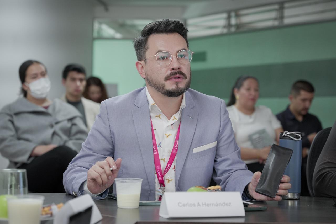 La imagen muestra a un hombre con gafas y un traje dando una presentación o charla a un grupo de personas sentadas.