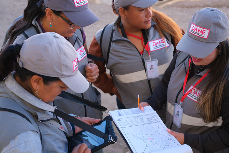 Tres censistas del DANE agrupadas revisando un mapa impreso en papel durante su recorrido.