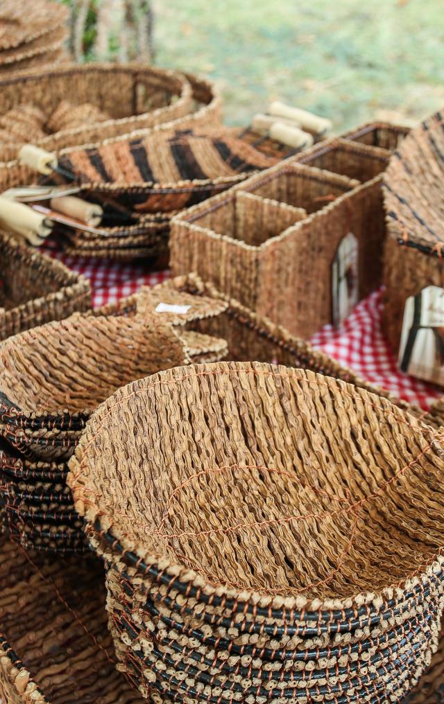 Variedad de canastos y recipientes tejidos en fibra natural con detalles negros, dispuestos en una mesa de mercado.