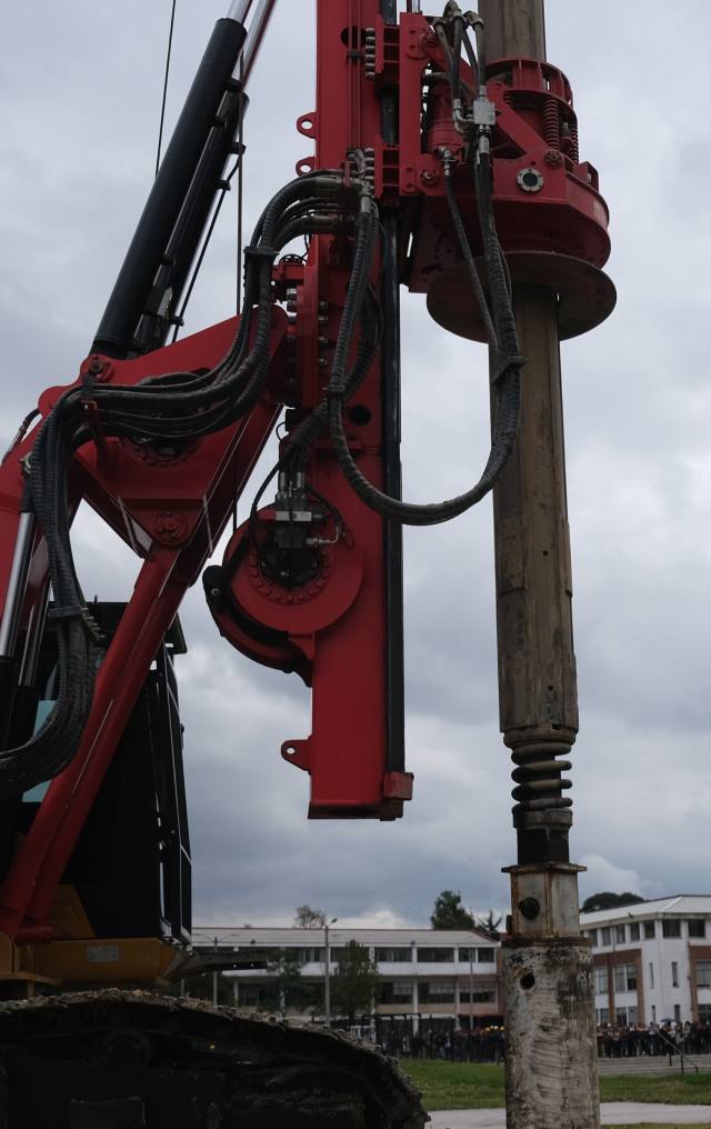 Maquinaria de perforación de color rojo en operación sobre pilotes de concreto en una obra de construcción con cielo nublado.