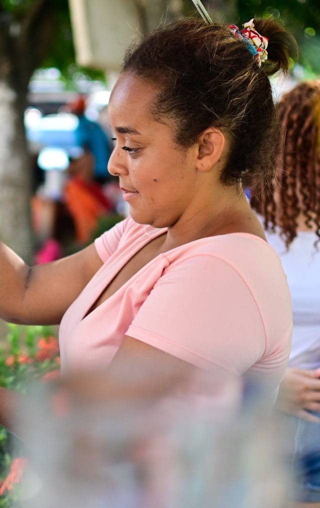 Mujer joven de perfil en un mercado al aire libre, con expresión serena y árboles al fondo.