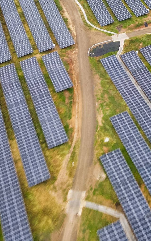 Vista aérea de un extenso campo de paneles solares fotovoltaicos con un camino de tierra que los atraviesa.